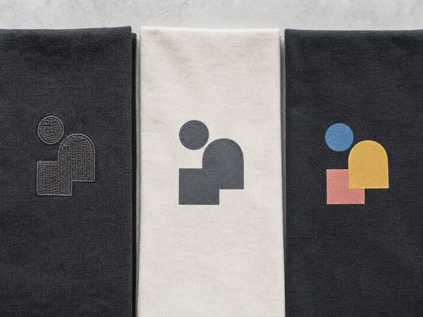 Photorealistic editorial image comparing embroidery, screen-print ink and DTF decoration on cotton fabric.