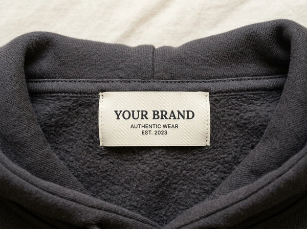 Custom branded woven neck label stitched into a charcoal hoodie collar — private label clothing by DenimByte