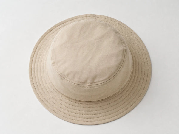 Photorealistic product mockup of a blank stone beige cotton twill bucket hat with concentric brim stitching viewed overhead.