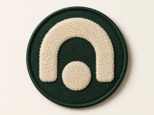 Photorealistic product mockup of an unbranded forest green and cream chenille patch with raised looped pile and a stitched edge.