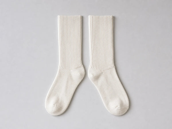 Photorealistic product mockup of a matching pair of blank off-white ribbed cotton crew socks viewed overhead on light grey.