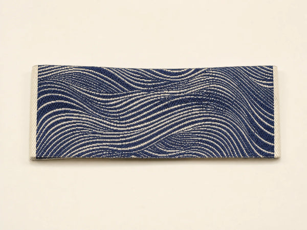 Photorealistic product mockup of a loose cream and navy damask woven garment label with fine abstract yarn detail.