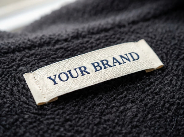 Custom damask woven clothing label in navy and cream, macro weave detail — woven labels for private label brands