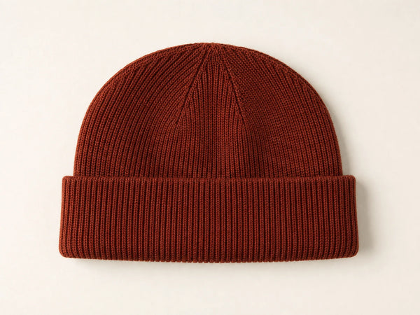 Photorealistic product mockup of a blank dark rust short fisherman beanie in a dense fine rib knit viewed overhead.