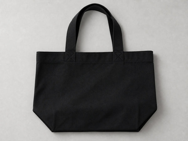 Photorealistic product mockup of a blank black heavyweight cotton gusseted tote bag viewed overhead on a light-grey background.