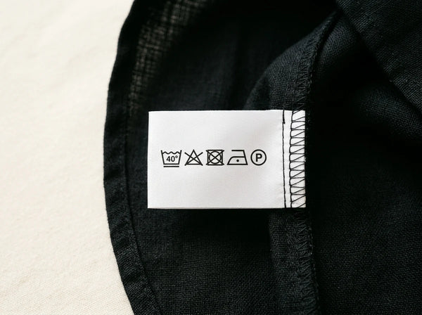 Printed care label with wash care symbols sewn into a black garment seam — custom care labels for clothing brands