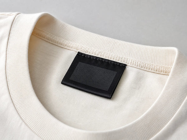 Photorealistic product mockup showing a blank black printed satin neck label sewn into an off-white T-shirt collar.