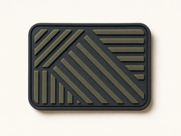 Photorealistic product mockup of an unbranded charcoal and olive flexible PVC patch with clean moulded relief.
