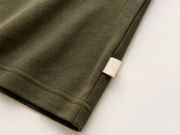 Photorealistic product mockup showing a blank cream woven side-seam label installed on an olive cotton T-shirt.
