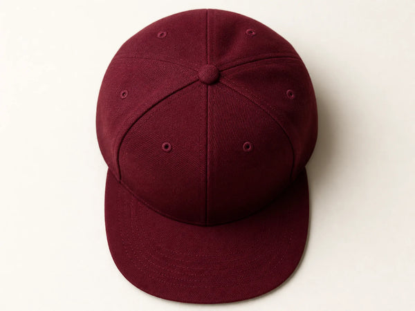 Photorealistic product mockup of a blank burgundy structured snapback cap with a flat brim viewed overhead on an off-white background.