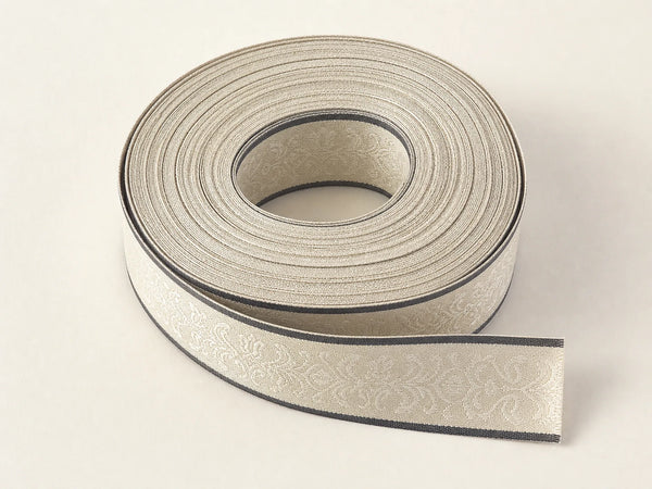 Photorealistic product mockup of a cream woven garment-label tape roll with charcoal borders and fine damask texture.