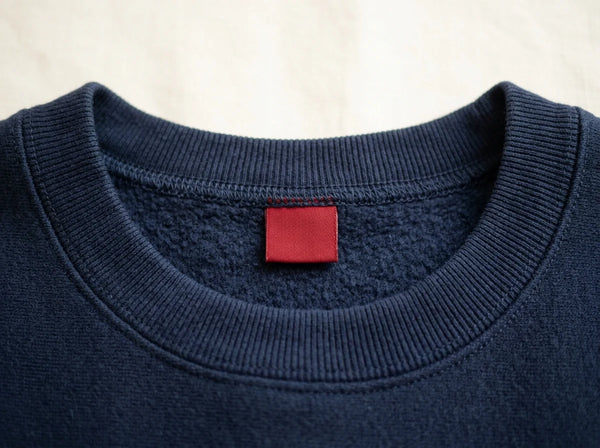 Colour-coded woven size tab in the collar of a navy sweatshirt — custom size labels for private label garments